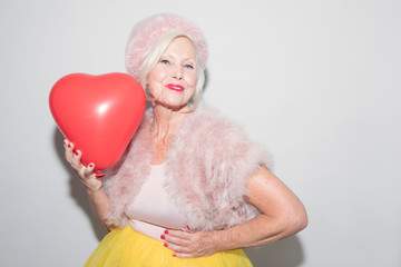 Portrait confident senior woman in fur holding heart-shape balloon