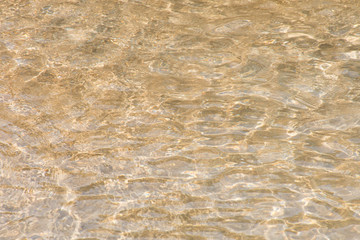 Water rippled and sunny reflections on the surface of gold sand in the sea.