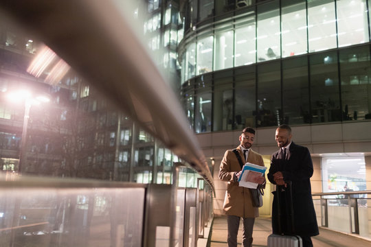 Businessmen suitcase discussing paperwork on urban pedestrian bridge at night