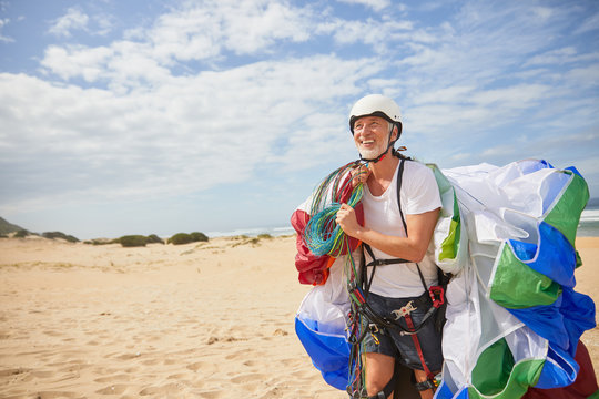 Smiling male paraglider carrying equipment parachute on sunny beach