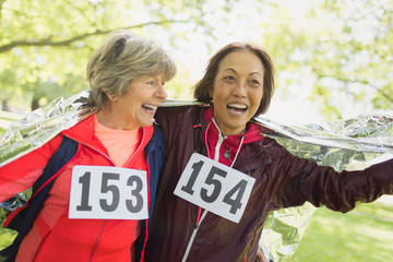 Happy active senior women finishing sports race, wrapped in thermal blanket