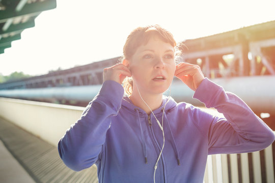 Young female runner adjusting headphones, listening to music