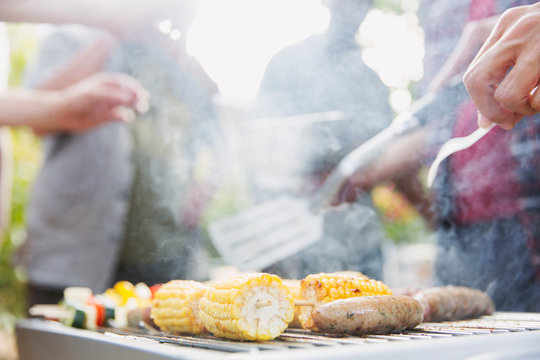 Corncobs, sausages and vegetable skewers cooking on barbecue grill
