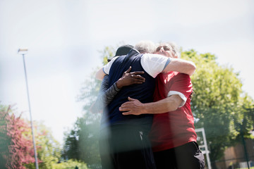 Active senior men friends hugging in sunny park