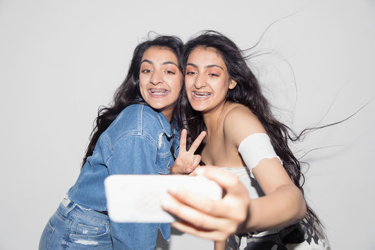 Carefree teenage twin sisters braces taking selfie smart phone