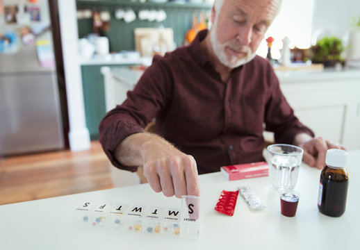 Senior Man Organizing Pill Box At Kitchen Table