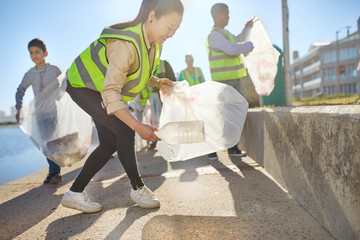 Woman volunteer picking up plastic litter on sunny boardwalk