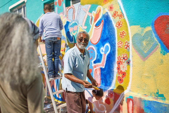 Senior man volunteer painting vibrant mural on sunny wall