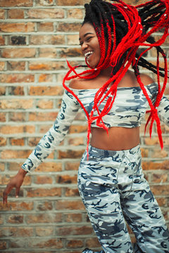 Carefree young woman in camouflage clothing dancing against brick wall