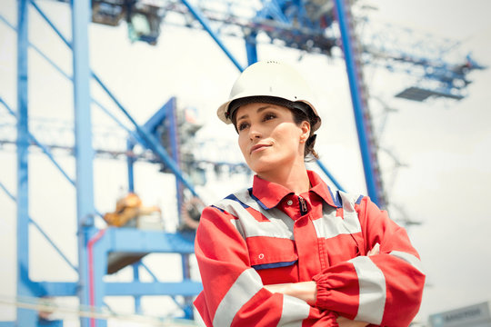 Confident female dock worker with arms crossed at shipyard