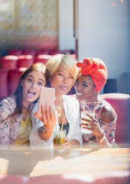 Silly, playful young women friends taking selfie camera phone in cafe