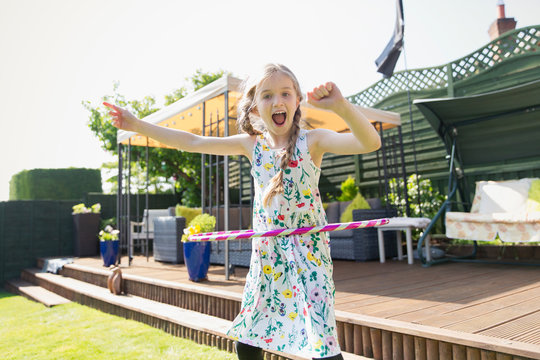 Portrait playful girl playing with plastic hoop in sunny back yard