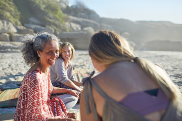 Smiling women friends talking on sunny beach during yoga retreat