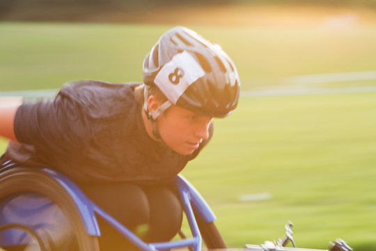 Determined young female paraplegic athlete speeding along sports track in wheelchair race