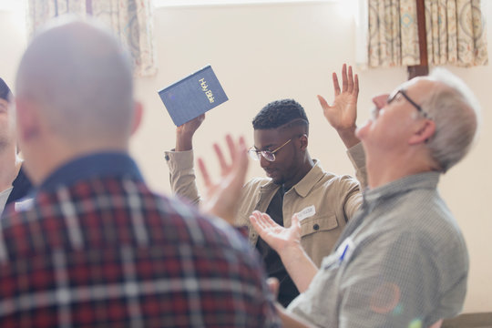 Men with bible praying with arms raised in prayer group