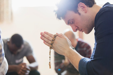 Serene man praying with rosary in prayer group