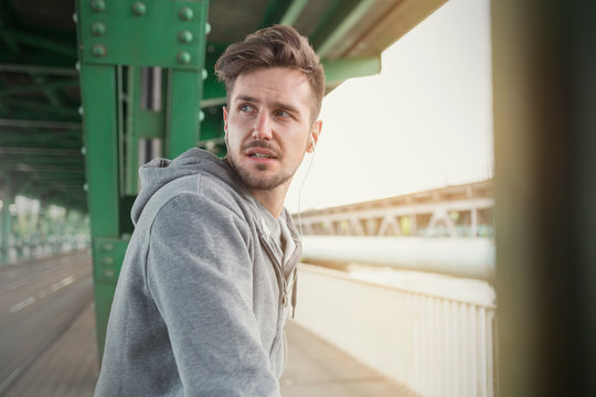 Young male runner with headphones looking over shoulder on train station platform