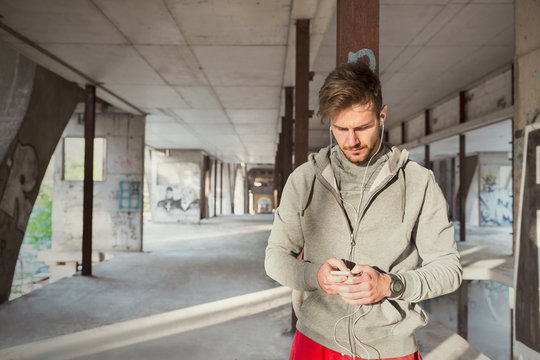 Young male runner listening music with mp3 player and headphones in abandoned building