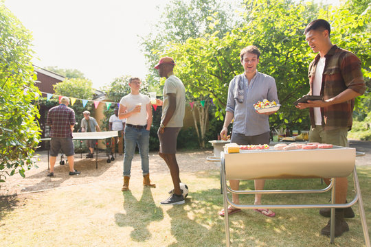 Male friends barbecuing in sunny summer backyard - Powered by Adobe