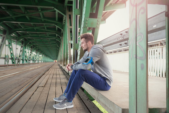 Young male runner resting on urban train station platform