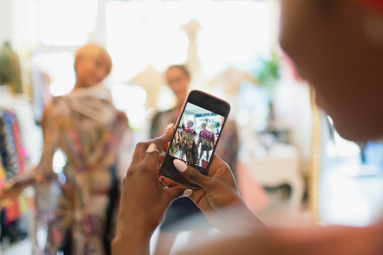 Young Woman With Camera Phone Photographing Friends Shopping In Store