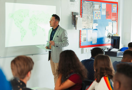 High school teacher leading geography lesson at projection screen in classroom
