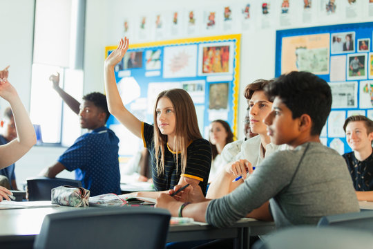 High school students with hands raised, asking questions during lesson in classroom