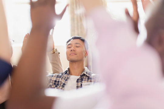 Serene man praying with arms raised in prayer group