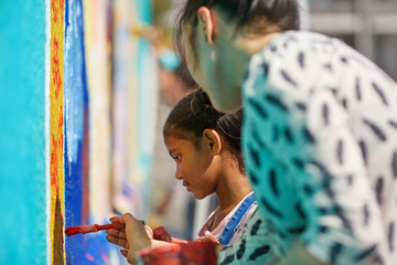 Teacher and elementary girl student painting on wall