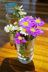 Purple and white flowers are blooming in glass on wooden desk at coffee shop.