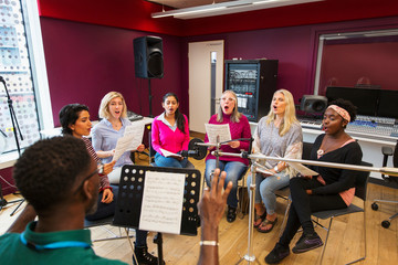 Womens choir with sheet music singing in music recording studio