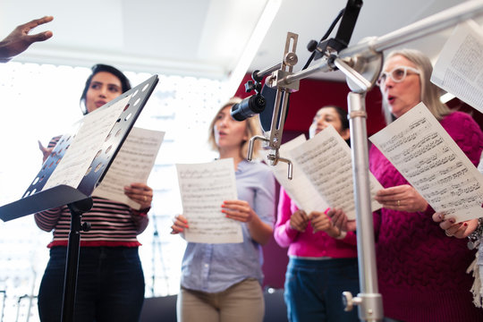 Womens choir with sheet music singing in music recording studio
