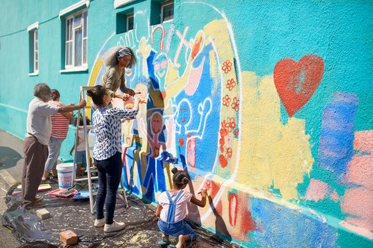 Community volunteers painting multicolor mural on sunny urban wall