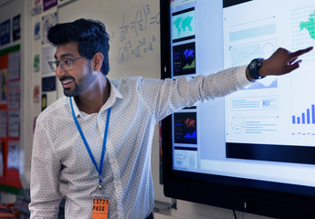 Smiling male teacher leading lesson at touch screen in classroom