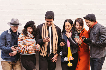 Fototapeta premium Young friends look in disgust at their smart phones - Diversity - Dressed in Winter Clothing in the daytime