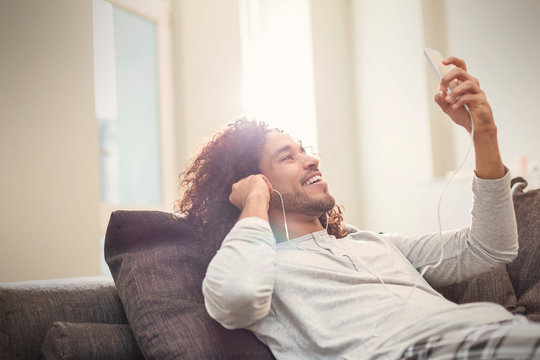 Smiling Young Man Relaxing, Listening To Music With Smart Phone And Headphones On Sofa