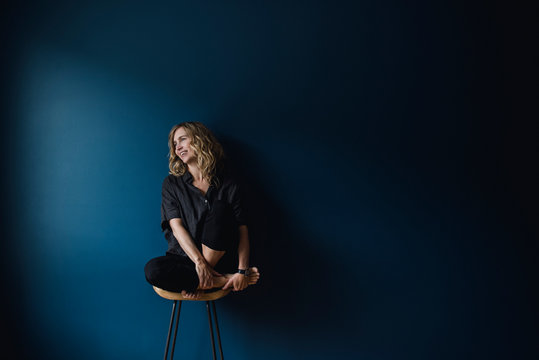 Portrait Carefree Woman Sitting On Stool Against Blue Background