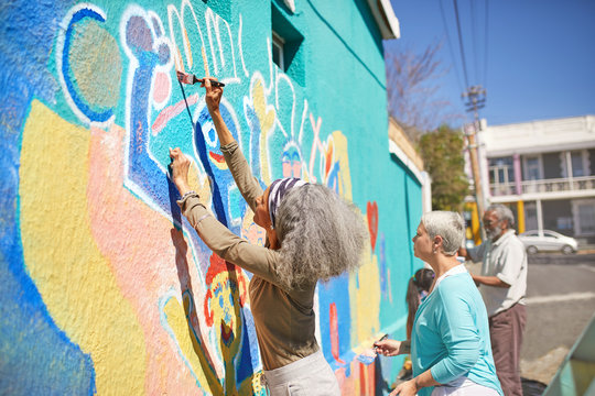Senior community volunteers painting vibrant mural on sunny urban wall