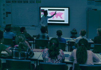 Students watching geography teacher at projection screen in dark classroom