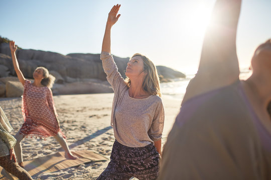 Serene woman practicing reverse warrior pose on sunny beach during yoga retreat