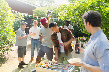 Male friends drinking beer and barbecuing in sunny summer backyard