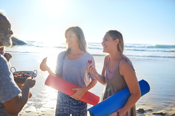 Mother daughter yoga mats eating fresh berries on sunny beach during yoga retreat