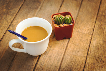 Coffee in a white mug with a beautiful cactus on a wooden table.