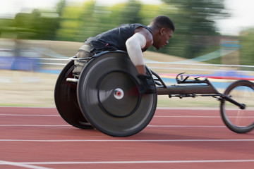 Determined young male paraplegic athlete speeding along sports track in wheelchair race