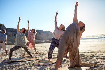 Group practicing yoga reverse warrior pose on sunny beach during yoga retreat