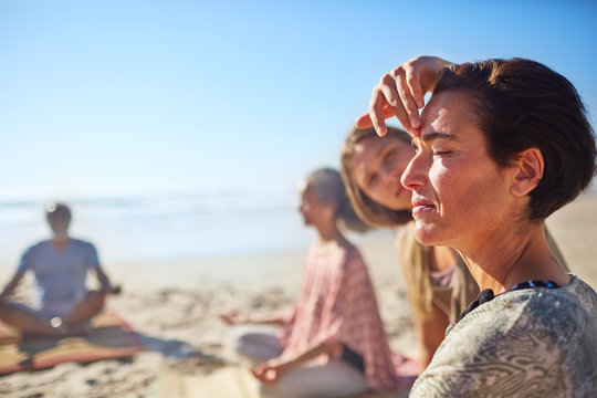 Yoga instructor touching third eye of woman meditating on sunny beach during yoga retreat