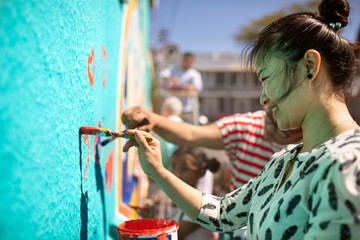Smiling female volunteer painting mural on sunny wall