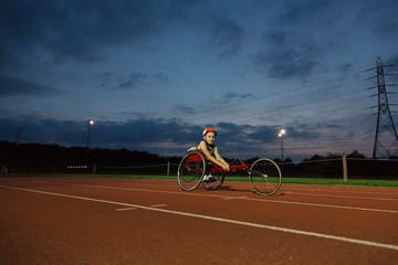Portrait confident teenage girl paraplegic athlete training for wheelchair race on sports track at night