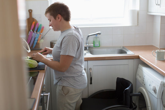 Woman with wheelchair cutting vegetables in apartment kitchen