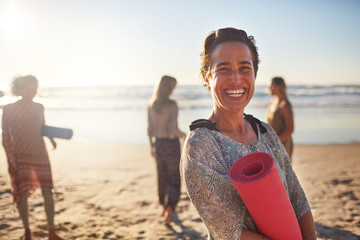 Portrait happy woman with yoga mat on sunny beach during yoga retreat